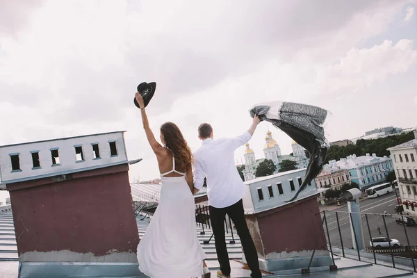 loving couple - a girl in a white dress with hat and a guy - on a walk on the roof hugging and laughing, a view from the roof of the city, positive and sincere emotions of love