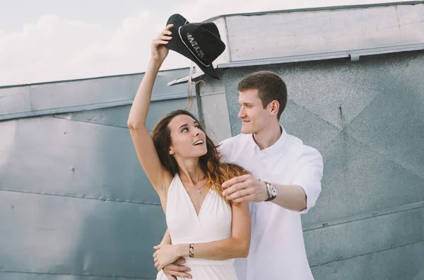 loving couple - a girl in a white dress and a guy with a hat - on a walk on the roof hugging and laughing,  positive and sincere emotions of love