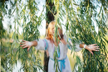 Nakış pozlar, yeşil ağaç bahar festivali ile beyaz Ulusal elbise sevimli sarışın kız