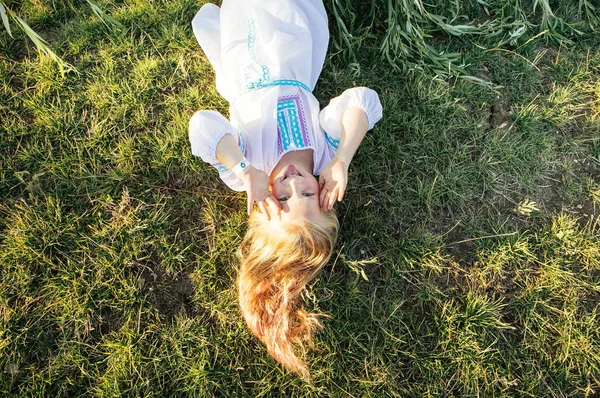 Nettes Blondes Mädchen Weißen Nationalkleid Liegt Auf Dem Gras Und — Stockfoto