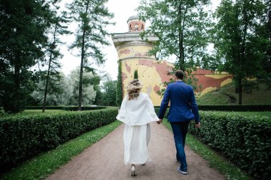 sarı duvar ve sarmaşık arka planına karşı bir yaz parkında yürürken eller tutarak ve gülümseyen onların düğün gününde şık gelin ve damat