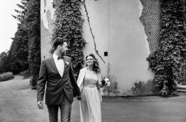 duvar ve sarmaşık, siyah beyaz fotoğraf arka planına karşı bir yaz parkında yürürken eller tutarak ve gülümseyen onların düğün gününde şık gelin ve damat