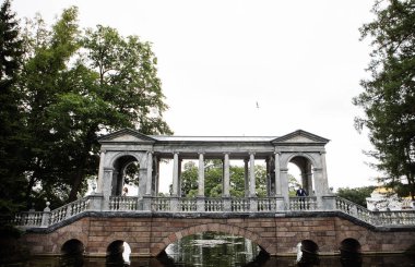 bir taş köprüde bir yazlık parkta yürürken kucaklayan ve gülümseyen düğün gününde şık gelin ve damat