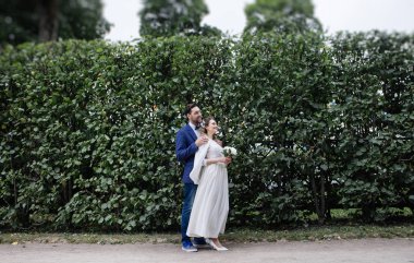 Düğün gününde sarılma ve bir bahar parkında gülümseyen şık gelin ve damat