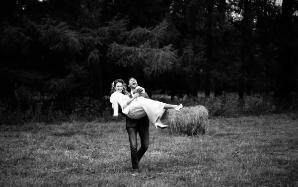 groom carrying his happy bride in arms in the field, an unusual wedding day, black and white photo