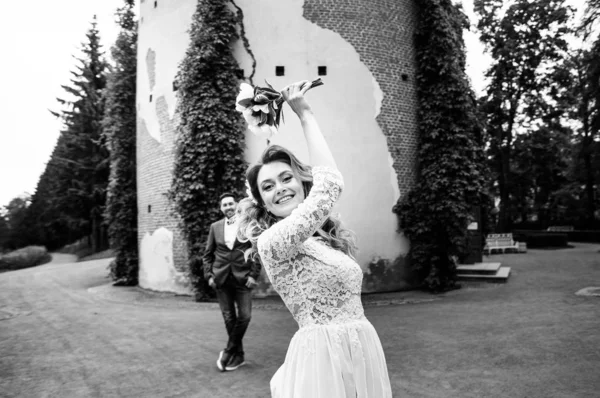 stylish bride throwing bouquet to groom in their wedding day in a summer park against the background of the wall and ivy, black and white photo