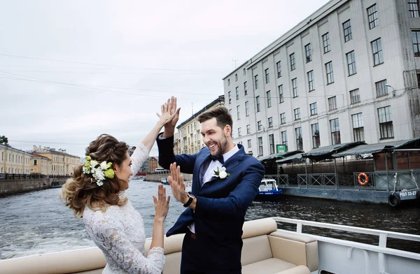 彼らの結婚式の日にスタイリッシュな新郎新婦は 川のボート旅行に楽しさとキスを持って — ストック写真