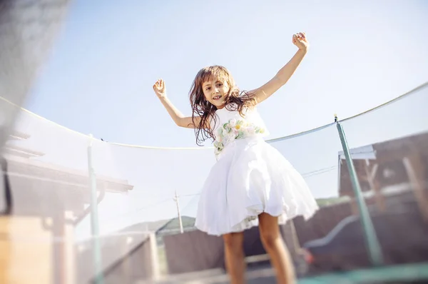 可爱的女孩在白色礼服有蹦床的乐趣 — 图库照片