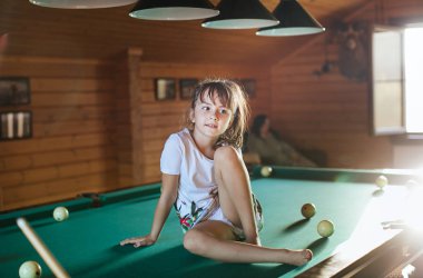 Küçük kız bilardo masasında oturuyor