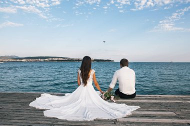 Mutlu genç gelin ve damat bir iskelede oturan, deniz manzarası zevk