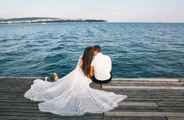 Mutlu genç gelin ve damat bir iskelede oturan, deniz manzarası zevk