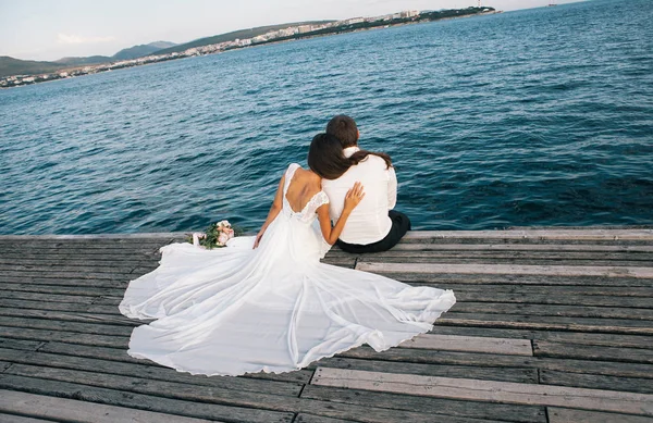 快乐的年轻新娘和新郎坐在码头上 享受海景 — 图库照片