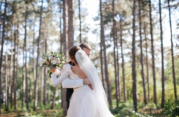 stylish and tender couple in love - the bride and groom - on their wedding day on a walk in the woods, laughing and hugging