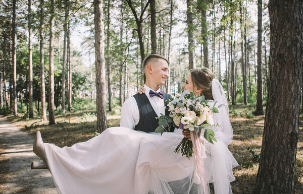 stylish and tender couple in love - the bride and groom - on their wedding day on a walk in the woods, laughing and hugging
