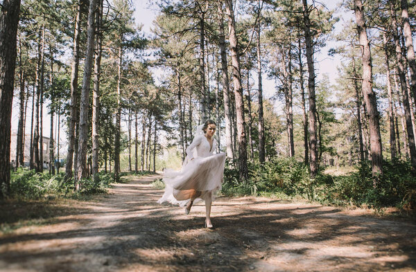 Tender young bride runs happy through the woods on the wedding day