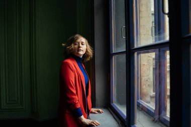 Kırmızı ceketli, mavi ceketli, pencerenin yanında mor çerçeveli, St. Petersburg 'da bir evde poz veren güzel sarışın kız.