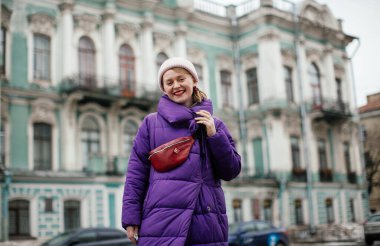 Mor ceketli, kırmızı kemerli sarışın St. Petersburg 'da yürüyor.
