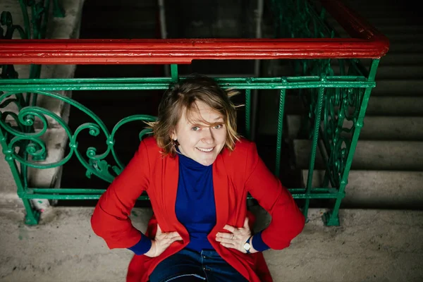 Colorful Blonde Girl Red Jacket Blue Jacket Sits Floor Entrance — Stock Photo, Image