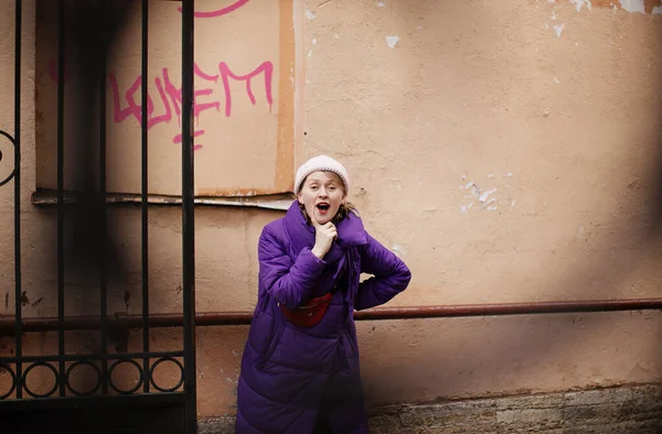 positive blonde in a purple down jacket and with a red belt bag walks around St. Petersburg