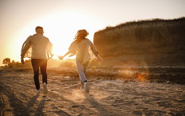 Kahverengi gömlekli şık bir çift nişandan sonra göl kenarındaki dağlarda yürüyüş yaparken mutlu erkek ve kız kucaklaşması, gün batımı.