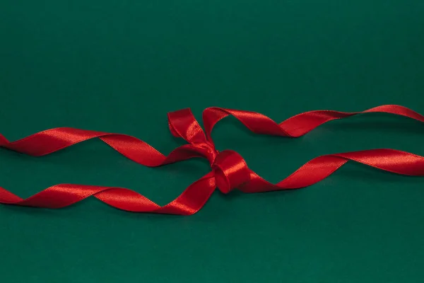 Decorative silk red ribbon with a bow on deep green background.