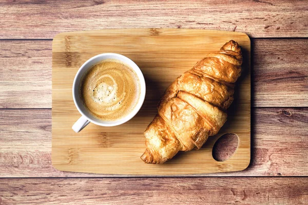 Perfect breakfast of croissant and coffee on wooden table. Rustic style.