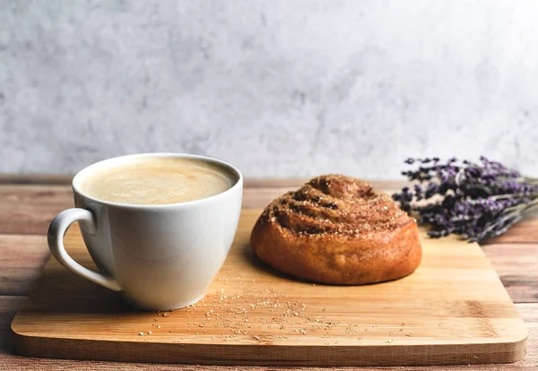 Perfect breakfast of homemade cinnamon bun and coffee on wooden table decorated with lavender. Rustic style.