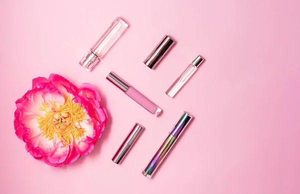 Flat lay composition with decorative makeup products, perfume and peony on pink background. Makeup and beaty concept.