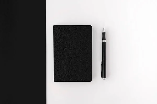Top view of closed black notepad with black fountain pen on black and white background. Mockup for your design.