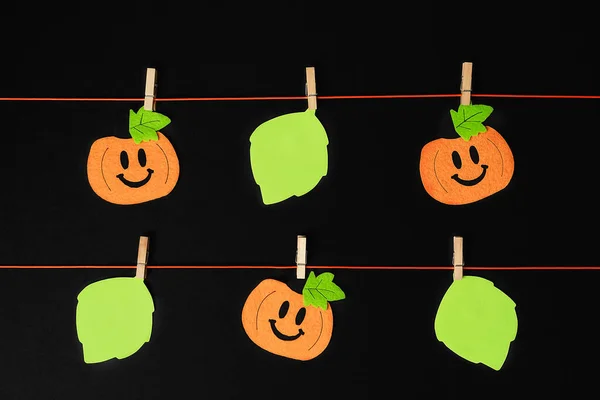 Background of halloween theme decorations. Toy pumpkins hanging on a string with wooden clothespins on black backdrop. Flat lay style. Copy space.