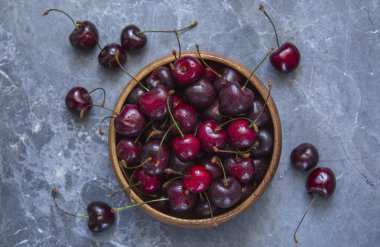 Olgun kiraz ile mavi mermer bir arka plan karşı ahşap bir kapta su damlaları.