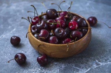 Olgun kiraz ile mavi mermer bir arka plan karşı ahşap bir kapta su damlaları.
