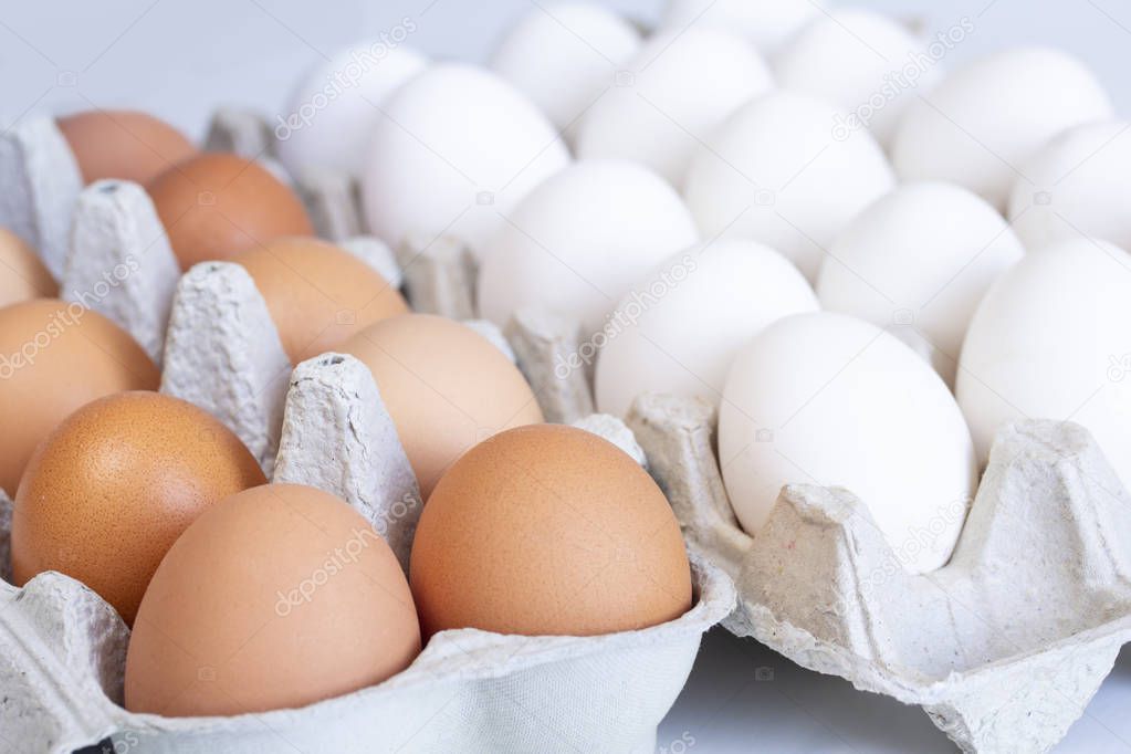 white and brown chicken eggs in an open cardboard tray on a white background
