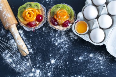 kek, yumurta içinde bir tepsi bir oklava ve un, siyah bir arka plan ile masada bir çırpma teli ile