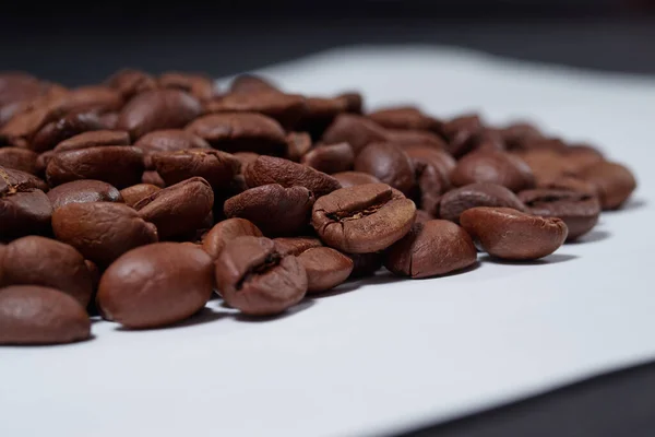 Vakre kaffebønner strødd på et hvitt bord med svart bakgrunn – stockfoto