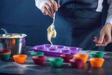 Şef pasta cupcake silikon kalıp koyu arka plan üzerinde içine hamur doldurarak bir siyah önlük. Şekerleme yemek kavramı