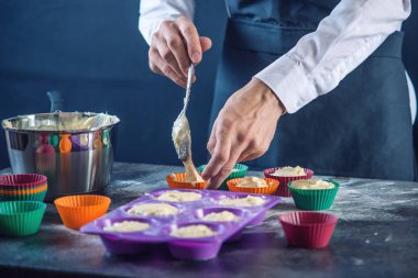 Şef pasta cupcake silikon kalıp koyu arka plan üzerinde içine hamur doldurarak bir siyah önlük. Şekerleme yemek kavramı