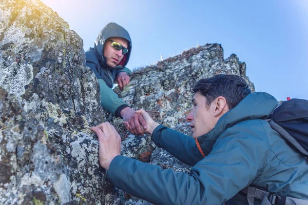 A man helps his friend to climb to the top. Hiker gives a hand to pull up the on mountain.