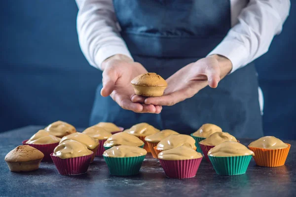 Chef pastry in a black apron holding the fresh baked muffins in hands. Concept of confectionery cooking