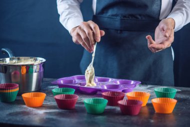 Şef pasta cupcake silikon kalıp koyu arka plan üzerinde içine hamur doldurarak bir siyah önlük. Şekerleme yemek kavramı