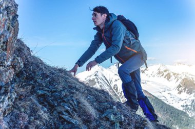 Adam arka plan karlı dağların üst için kayalık kayaların üzerinde sürünerek bir sırt çantası ile Hiking. Kavram zor yolu ve hedef başarı