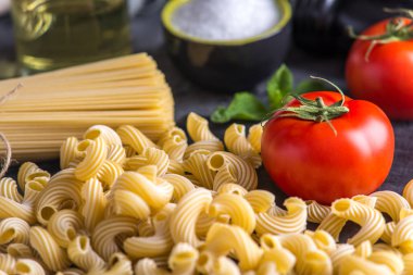 Pişmemiş makarna çeşitleri fırıncı ve spagetti için karanlık bir arka plan üzerine domates sosu malzemeler ile. Gıda tasarım kompozisyon kavramı.