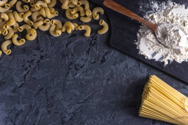 Pişmemiş İtalyan makarna spagetti ve fırıncı ile karanlık bir arka plan üzerinde makarnalık buğday unundan. Gıda tasarım kompozisyon kavramı.