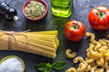 Pişmemiş makarna çeşitleri fırıncı ve spagetti için karanlık bir arka plan üzerine domates sosu malzemeler ile. Gıda tasarım kompozisyon kavramı.