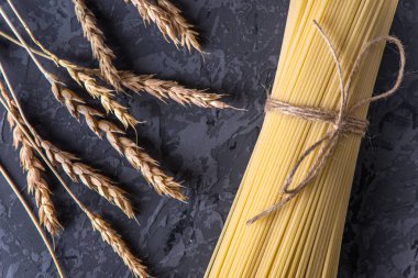 Pişmemiş İtalyan makarna spagetti ve fırıncı ile karanlık bir arka plan üzerinde makarnalık buğday spikelets. Gıda tasarım kompozisyon kavramı.