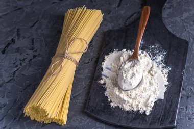 Pişmemiş İtalyan makarna spagetti ve karanlık bir arka plan üzerinde makarnalık buğday unundan ile. Gıda tasarım kompozisyon kavramı.