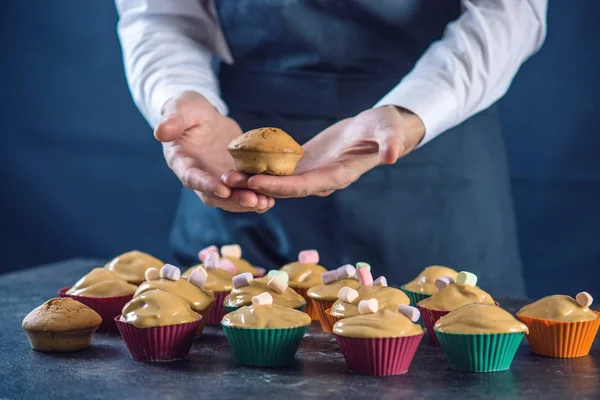 Chef pastry in a black apron holding the fresh baked muffins in hands. Concept of confectionery cooking