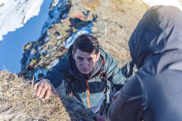 A man helps his friend to climb to the top. Hiker gives a hand to pull up the on mountain.