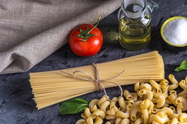 Pişmemiş makarna çeşitleri fırıncı ve spagetti için karanlık bir arka plan üzerine domates sosu malzemeler ile. Gıda tasarım kompozisyon kavramı.