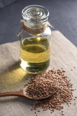 Bir yığın kaşık ve keten tohumu Keten tohumu altın cam şişe masanın üzerinde karanlık bir arka plan üzerinde yağda. Omega 3 yağ asitleri ile kavram sağlıklı beslenme.